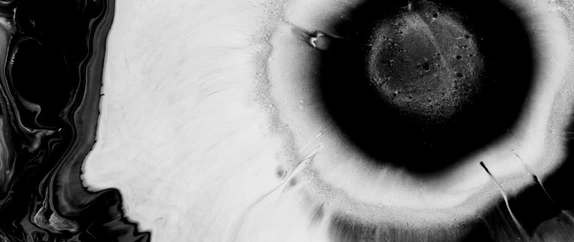 A drop of white liquid creates a circular expanding shape replacing the dark liquid flow around it