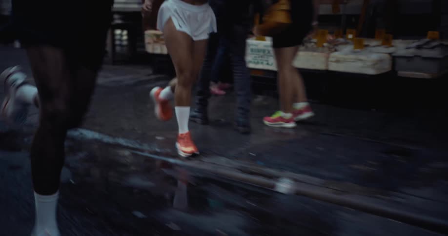 A man and a woman jogging together on a city street running past pedestrians and boxes of produce on the sidewalk