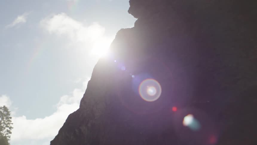 Reflection of the sun hitting a rocky wall of a mountain with conifers in the background