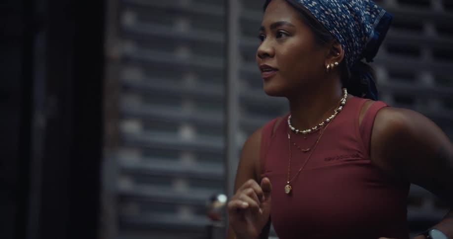 Closeup of a woman wearing a red sleeveless top and a blue patterned headscarf as she jogs past a metal shutter