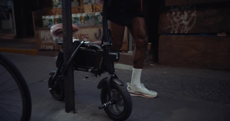 Man jogs along the sidewalk past a very small electronic bike and a cyclist walking his bicycle