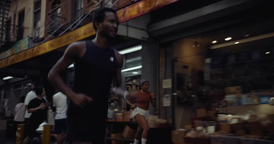 Two people are jogging on a bustling city street weaving around pedestrians on the sidewalk