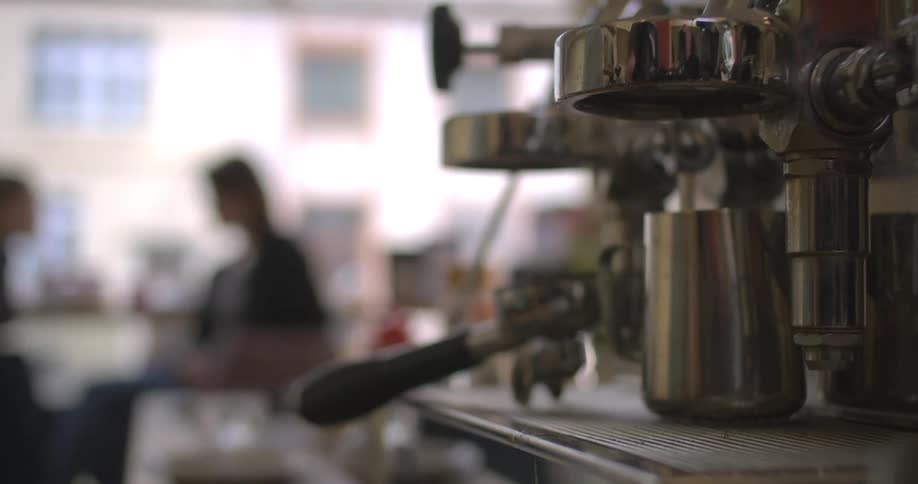 A person is operating an espresso machine removing a portafilter into the group head likely preparing to brew coffee