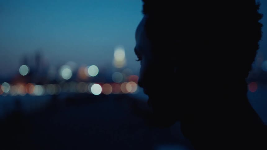 A silhouette of a person is seen against a waterfront city skyline at dusk