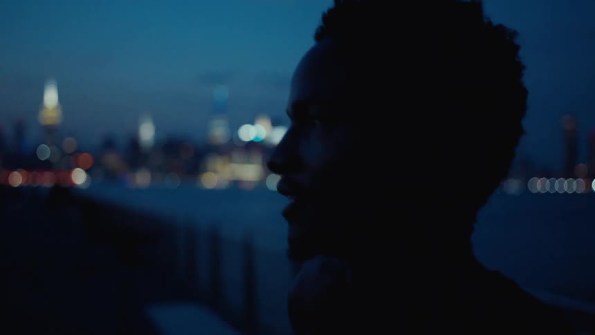 A silhouette of a person is seen against a waterfront city skyline at dusk