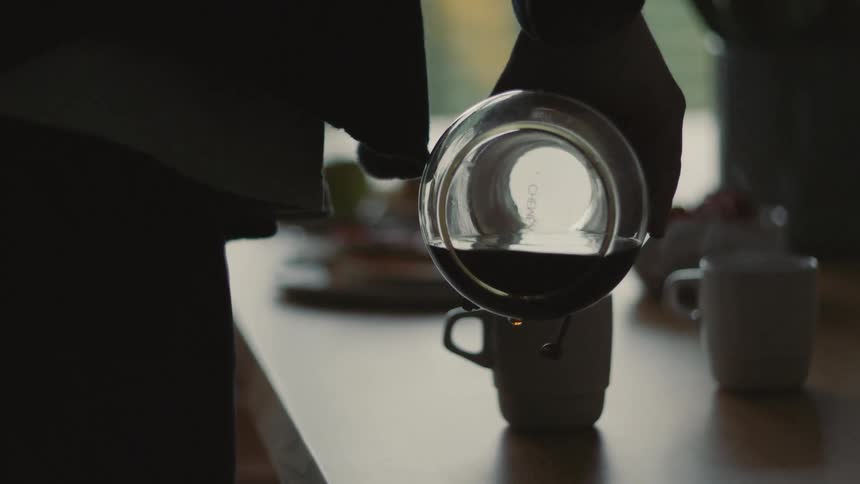 Person serving coffee into two white ceramic mugs