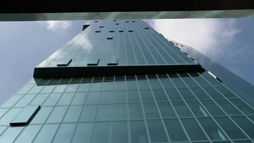 Upward view of a modern skyscraper against a blue sky with few clouds