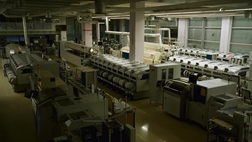 A flashlight beam sweeps over an industrial manufacturing facility with large machines and equipment arranged in rows for automated production processes