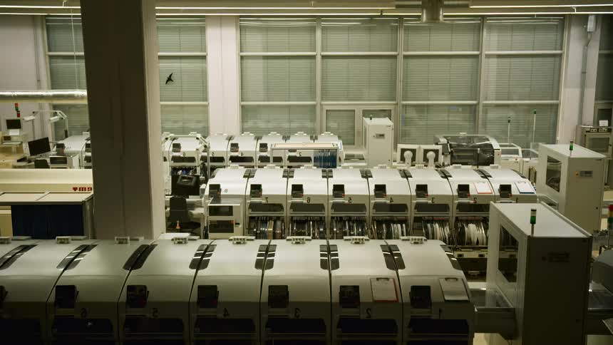 A flashlight beam inspects a brightly lit factory interior showcasing rows of automated machinery lined up in an assembly line