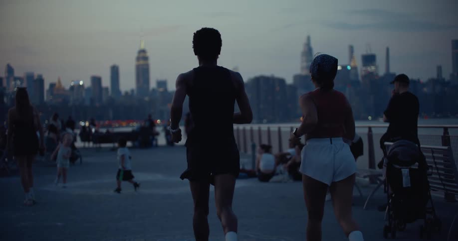 Woman and a man running along a pier with a cityscape in the background