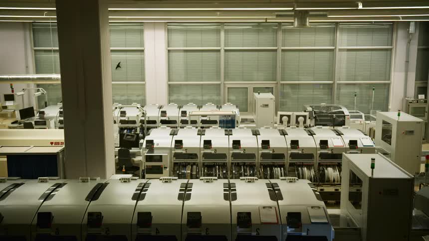 A flashlight beam sweeps over an industrial manufacturing facility with large machines and equipment arranged in rows for automated production processes