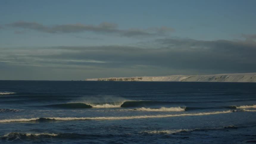 Ocean waves splashing on shore near a rocky snowy coast