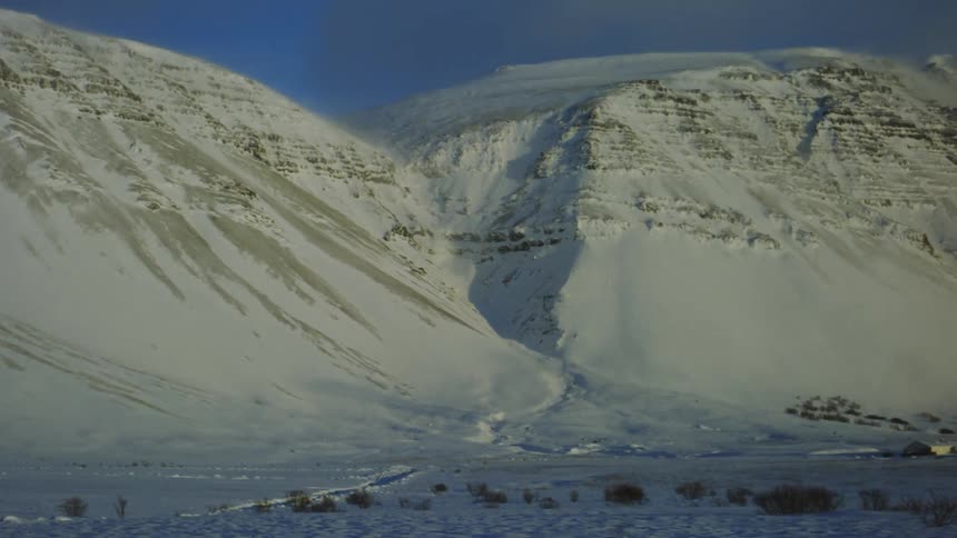 A snowcovered mountainous landscape with steep slopes and ridges featuring patches of exposed rock and a valley at the base