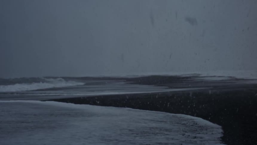 Snow falls on a desolate windswept beach under a gray overcast sky