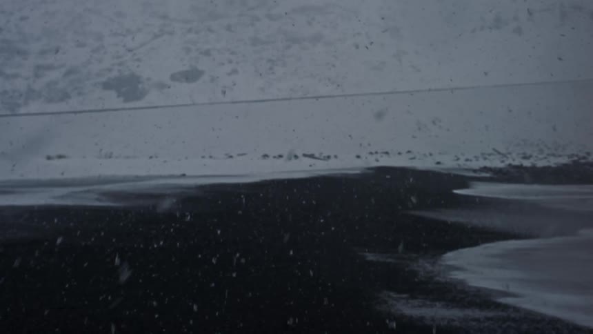 Snow falling heavily on a dark wet landscape near a snow covered road