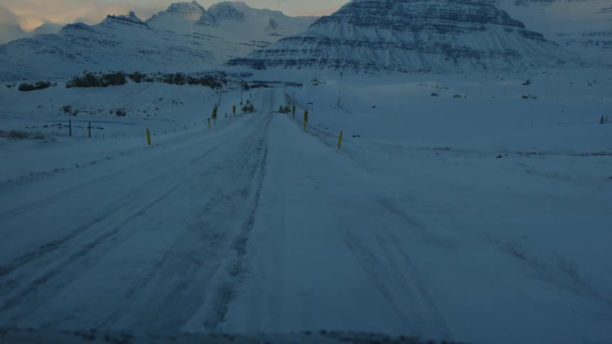 A road covered in white snow and in the background there are some huge mountains also full of snow