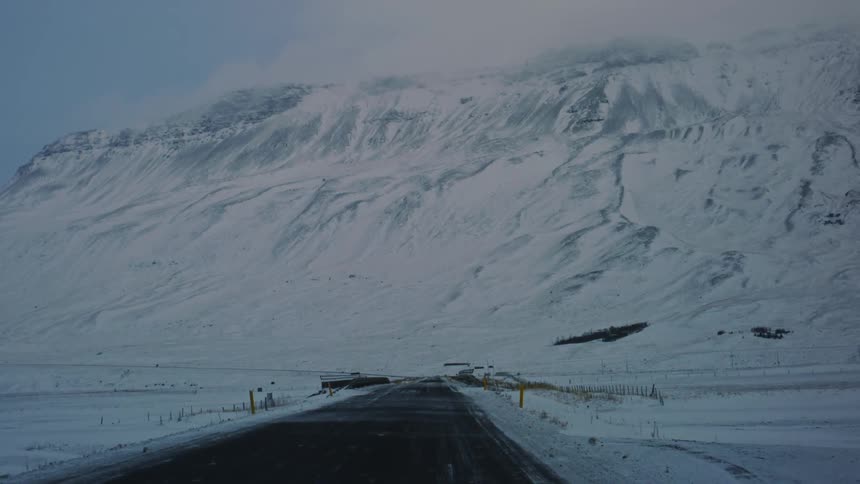 Paved road leads towards a large snowcovered mountain under a cloudy sky