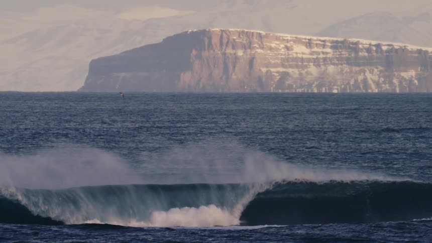 Large wave in a sea with mountains in the background
