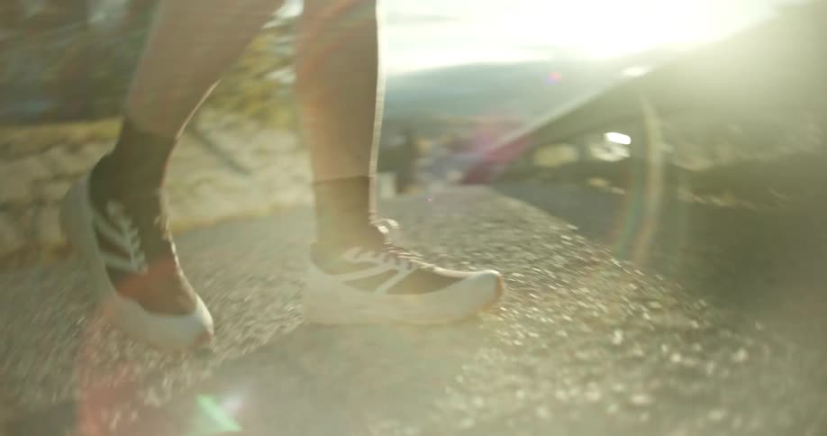 In a closeup shot a persons shoes tread uphill at sunrise with a distant mountain in the horizon and golden sunlight reflecting off a nearby guardrail