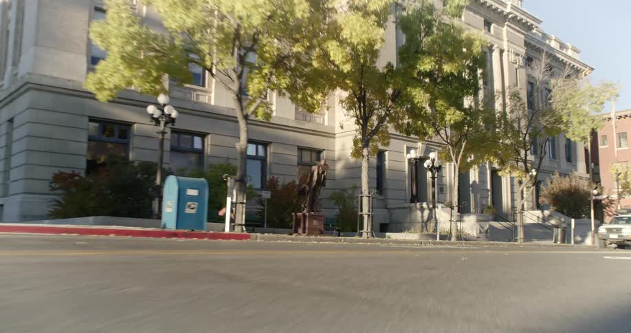 A person runs along a city street in front of a large classic building and trees