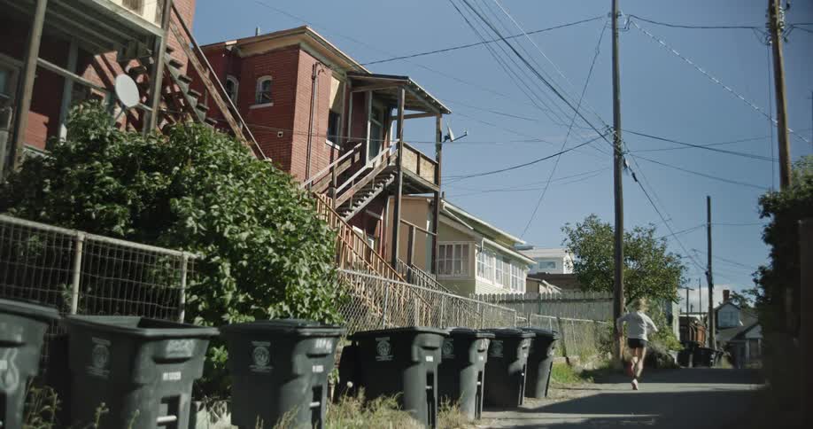 A blonde woman runs down a side street in a residential neighborhood on a sunny summer day