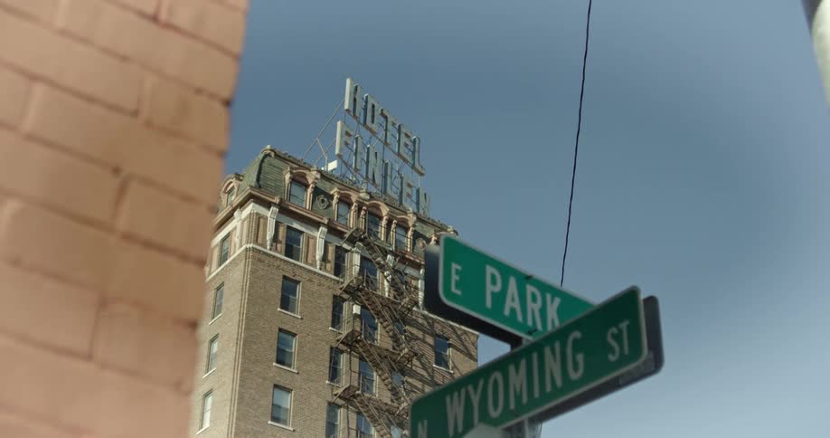 Old building with a hotel sign on top is seen in the background while street signs indicate the intersection of e park and wyoming st