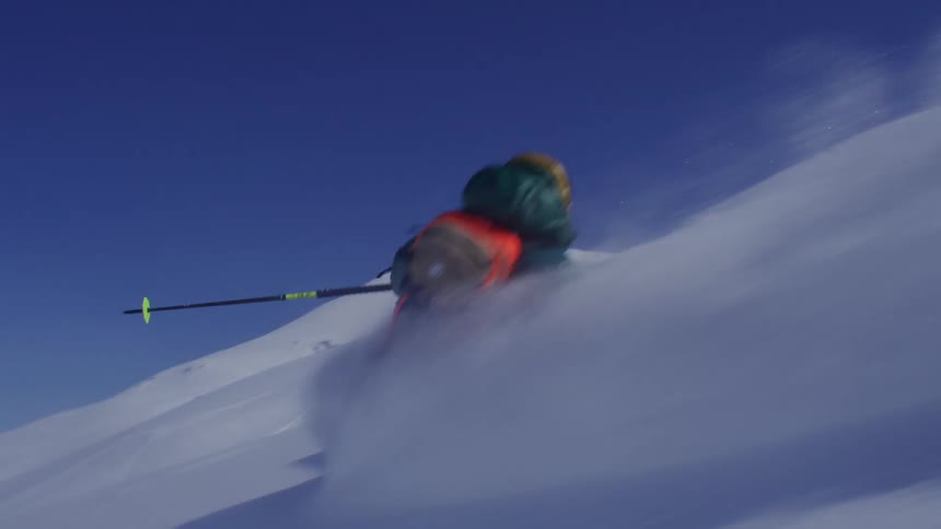 A skier in light blue pants and a dark jacket is falling on a snowy slope under a blue sky