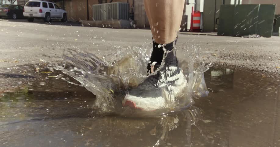 A person runs on the city street stepping into a puddle and splashing water
