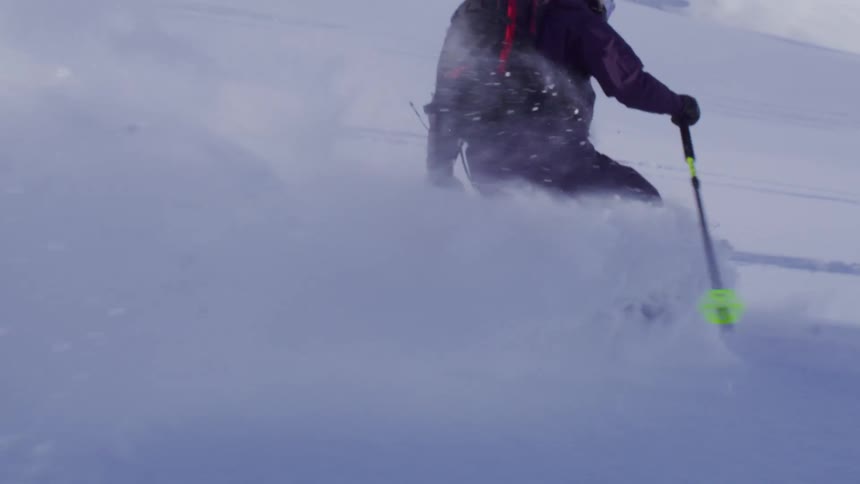 A person is skiing through deep snow on a mountainous terrain wearing a helmet and carrying a backpack