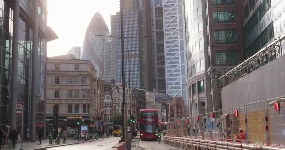 A red double decker bus speeds down a london street with iconic skyscrapers in the background