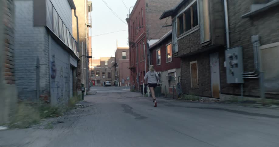A blonde woman runs down an alley in an urban area on a sunny day