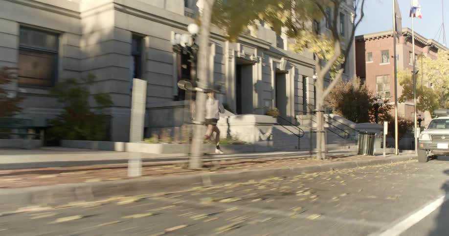 A blonde woman runs down the sidewalk in an urban area on a sunny autumn day