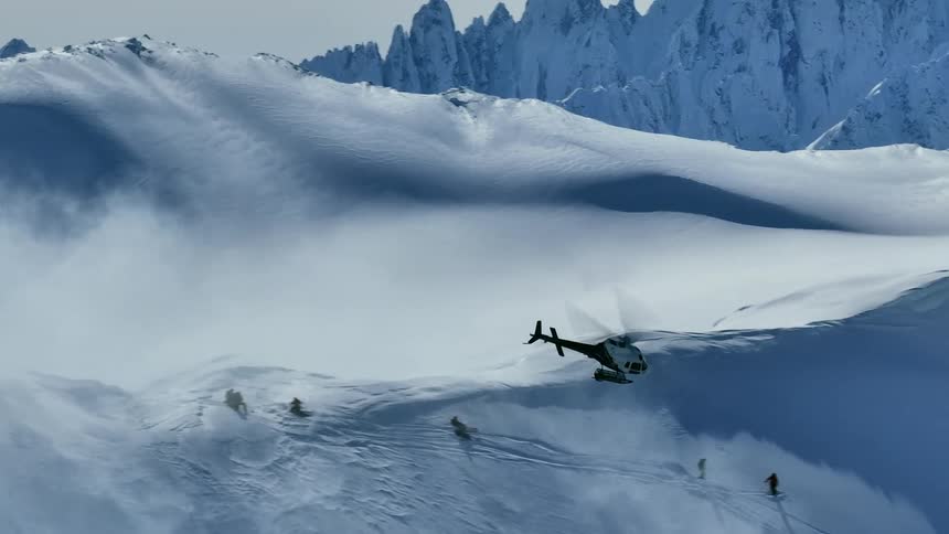 Helicopter flies over snowy mountains as skiers descend the slope