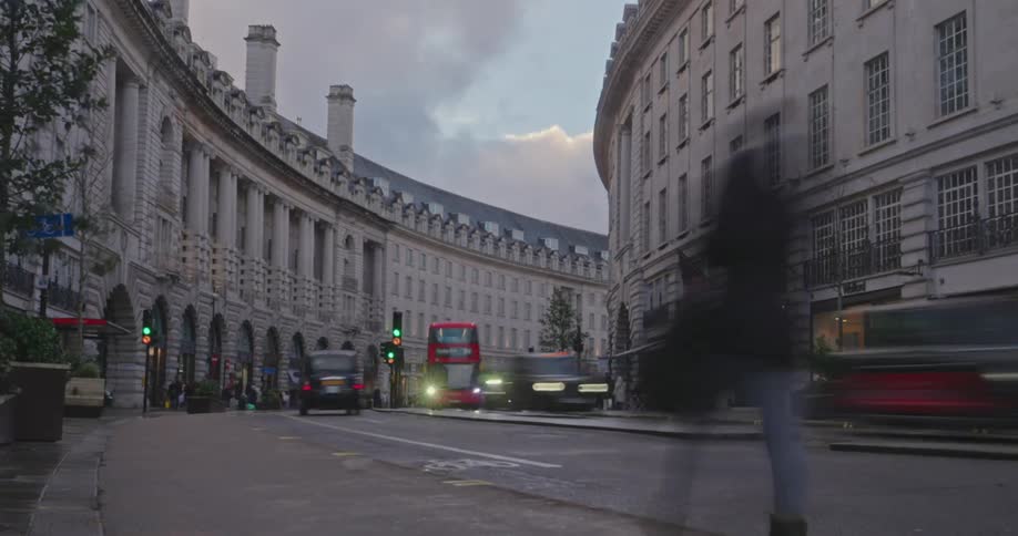Time lapse of traffic and pedestrians on a curved street lined with classic ornate buildings under an overcast sky