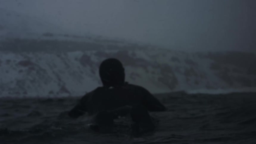 Surfer wearing a wet suit paddles on his board on a winter day during a storm