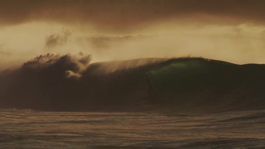 Person is surfing on huge waves in the ocean water at dusk