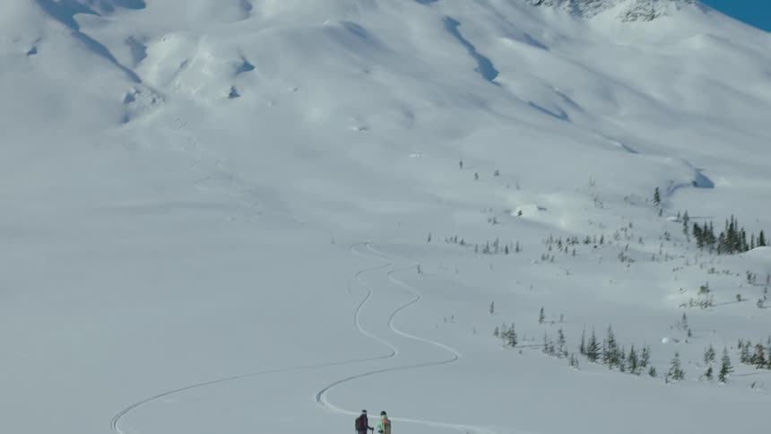 Two people stand in a vast snowy landscape following a winding trail marked on the white surface