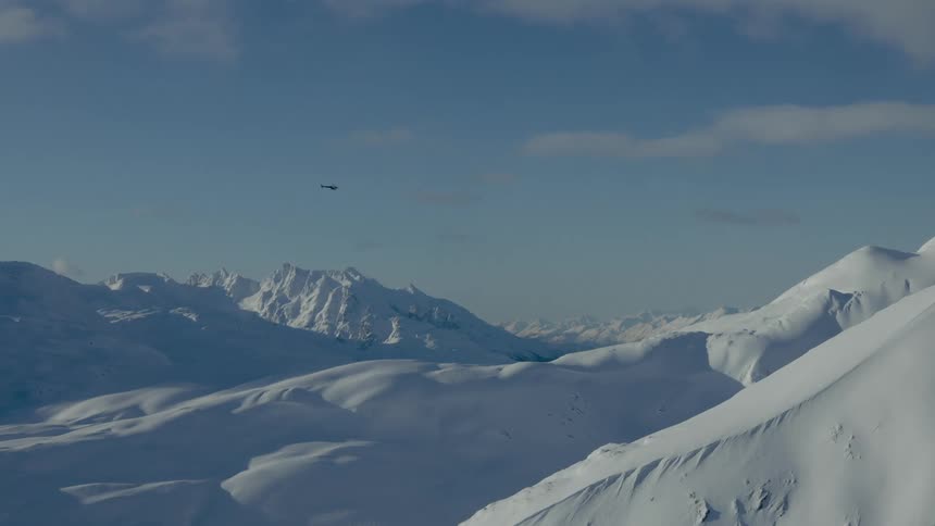 Helicopter is flying above snow covered mountaintops