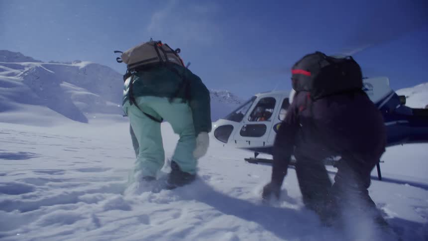 Two people are walking towards a helicopter during a winter storm