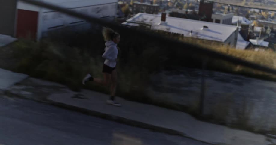 A woman is running downhill on a steep sidewalk with a cityscape in the background