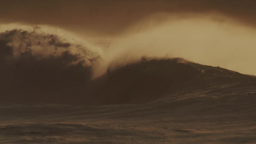 A big sea wave breaking next to some surfers who are moving away from it