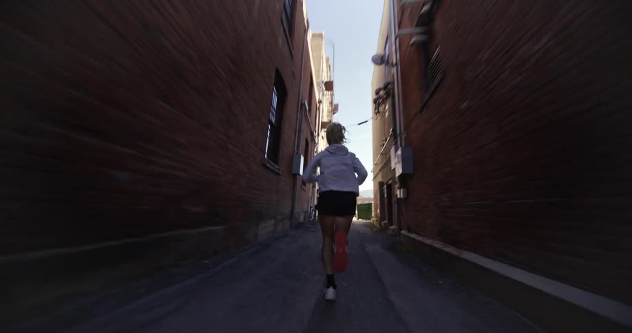 A woman is running down a narrow alleyway between two brick buildings