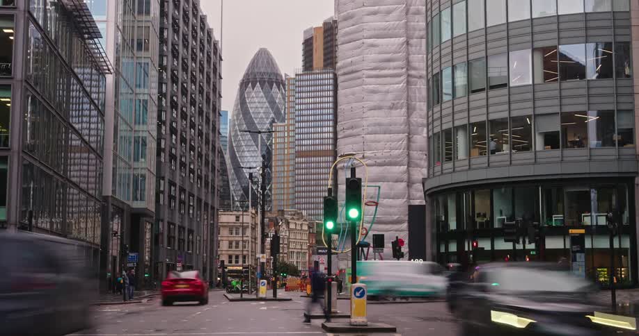 Busy street in london shows red traffic lights a red doubledecker bus motorcyclists and pedestrians with the gherkin building in the background