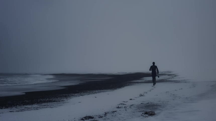 A person is jogging along side the coast of a beach in winter