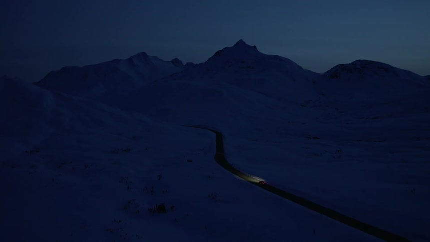 Car drives along a lonely road surrounded by snowcapped mountains at night