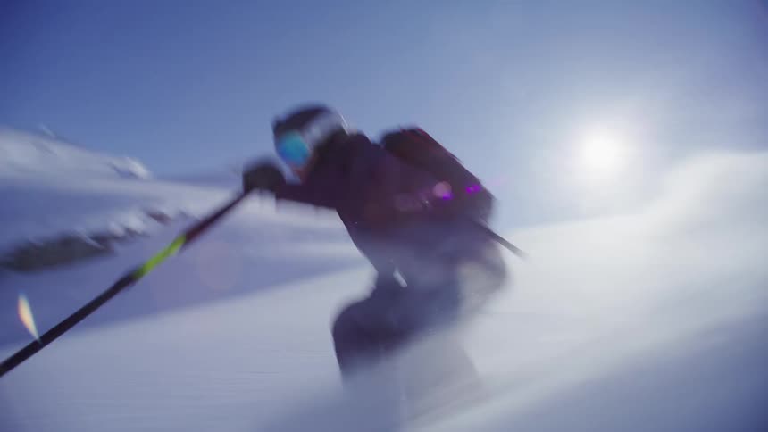 A skier is skiing down a snowy slope with a clear blue sky and the sun shining brightly in the background