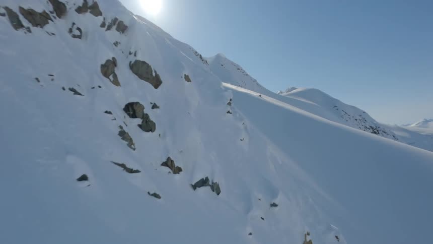 Person skis alone across a vast landscape of snowcapped mountains under a clear blue sky