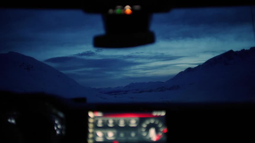 View from inside a car at night showing an illuminated dashboard in contrast with the icy landscape in the background