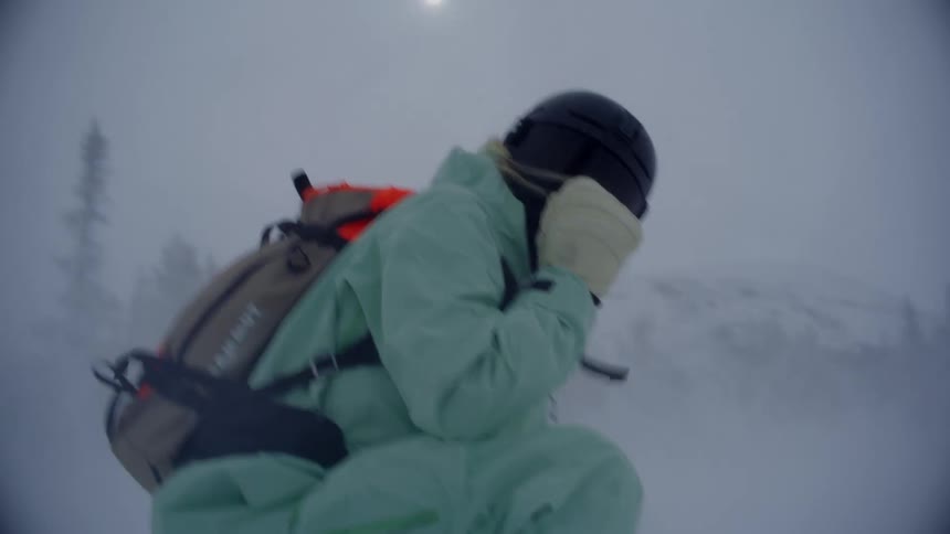 Woman wearing thermal clothing and a helmet protects herself from strong winds and heavy snow as she braves a storm in a mountainous environment covered in fog