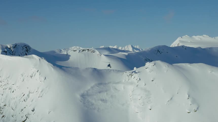 A helicopter blows the snow around on top of the mountain
